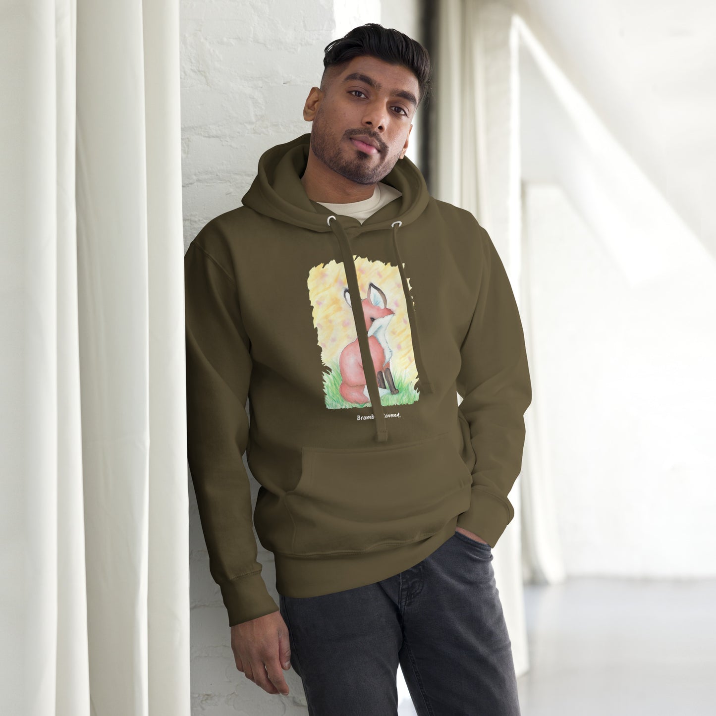 Unisex military green colored hoodie. Features original watercolor painting of a fox in the grass against a yellow backdrop. Shown on male model.
