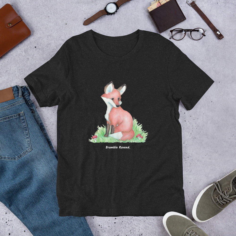 Unisex black heather colored forest fox t-shirt. Features watercolor print of a fox in the grass surrounded by mushrooms and ferns.