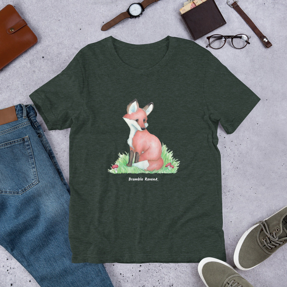 Unisex heather forest green colored forest fox t-shirt. Features watercolor print of a fox in the grass surrounded by mushrooms and ferns.