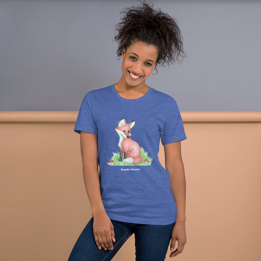 Unisex  heather true royal blue colored forest fox t-shirt. Features watercolor print of a fox in the grass surrounded by mushrooms and ferns. Shown on female model.