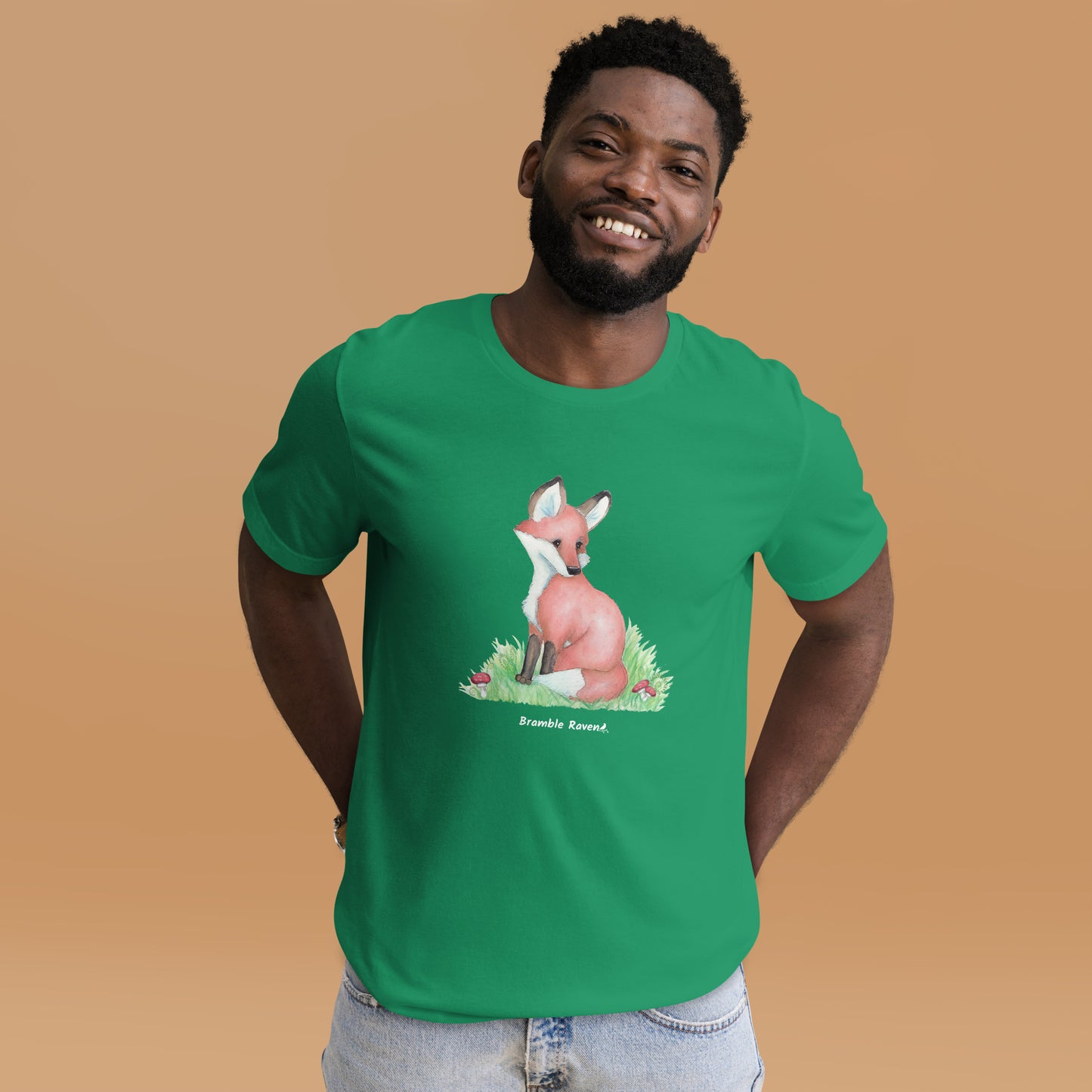 Unisex kelly green colored forest fox t-shirt. Features watercolor print of a fox in the grass surrounded by mushrooms and ferns. Shown on male model.