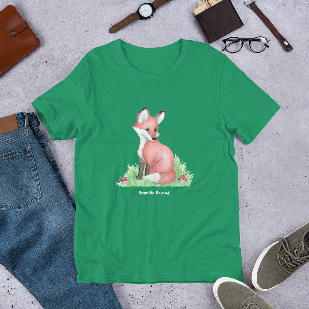 Unisex kelly green colored forest fox t-shirt. Features watercolor print of a fox in the grass surrounded by mushrooms and ferns.