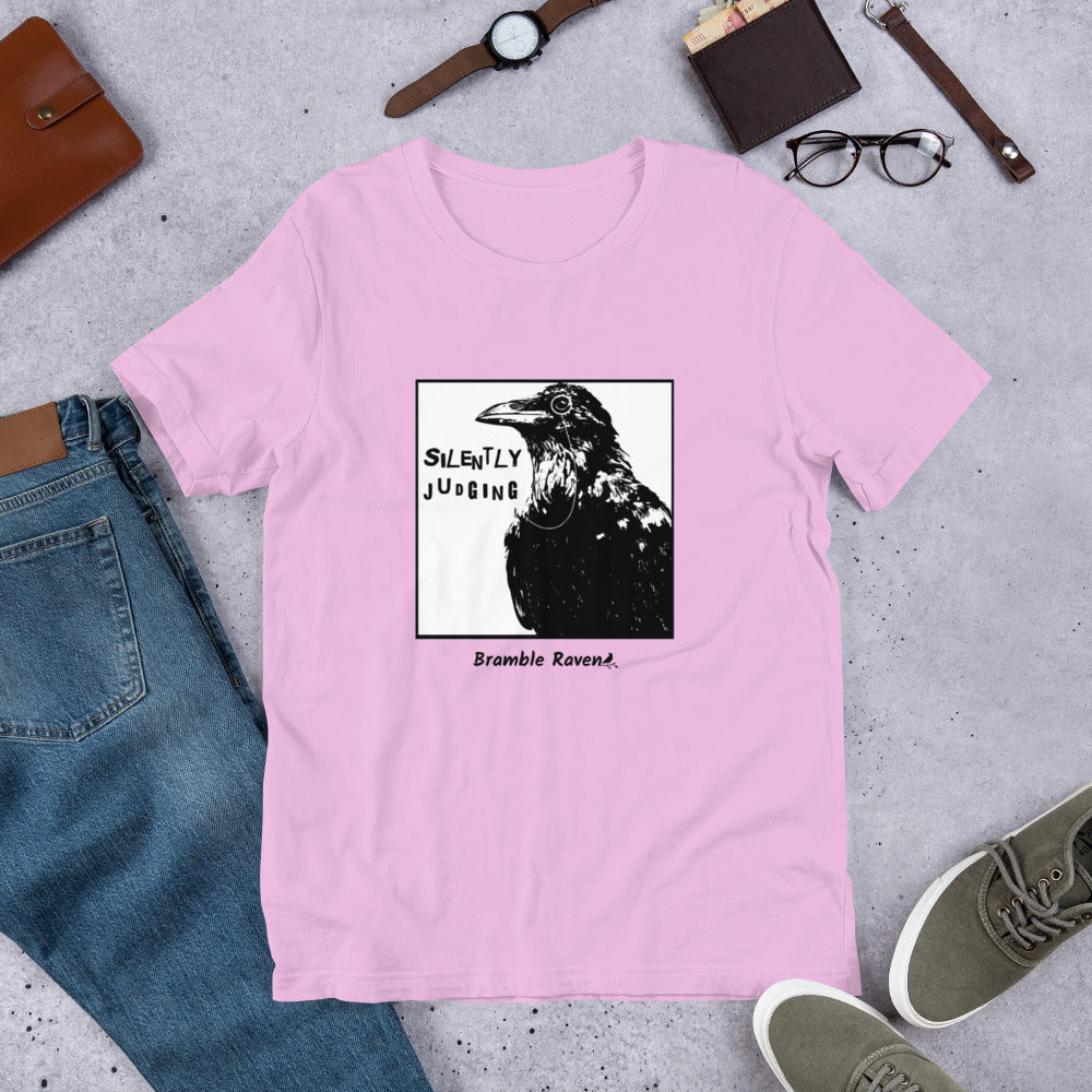 Unisex pink colored t-shirt. Features silently judging text next to black crow wearing a monocle in a square frame on a white background. 