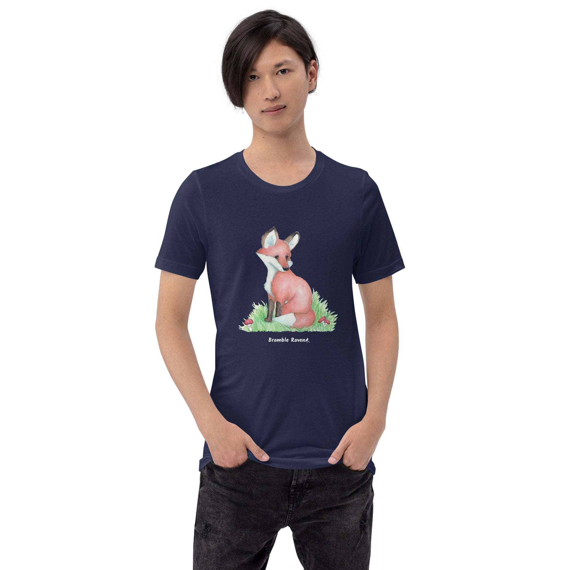 Unisex navy blue colored forest fox t-shirt. Features watercolor print of a fox in the grass surrounded by mushrooms and ferns. Shown on male model.