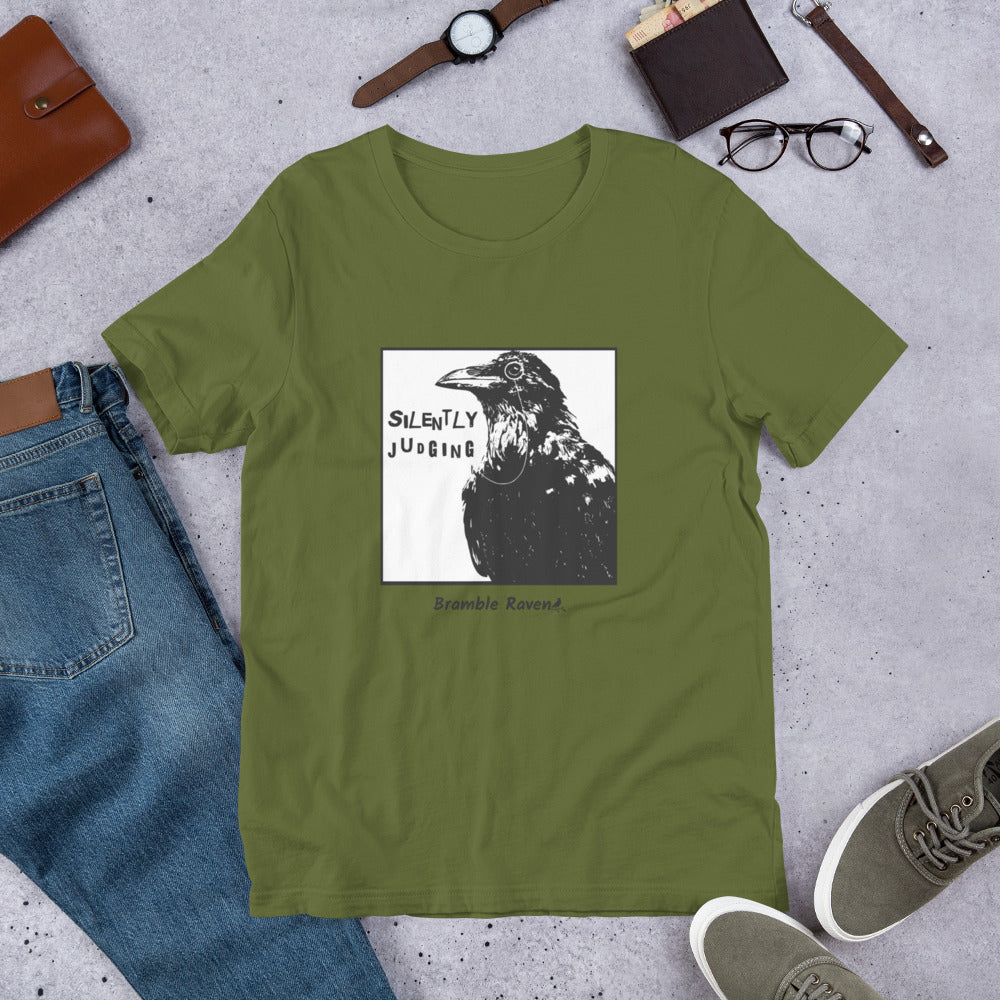 Unisex olive green colored t-shirt. Features silently judging text next to black crow wearing a monocle in a square frame on a white background. 