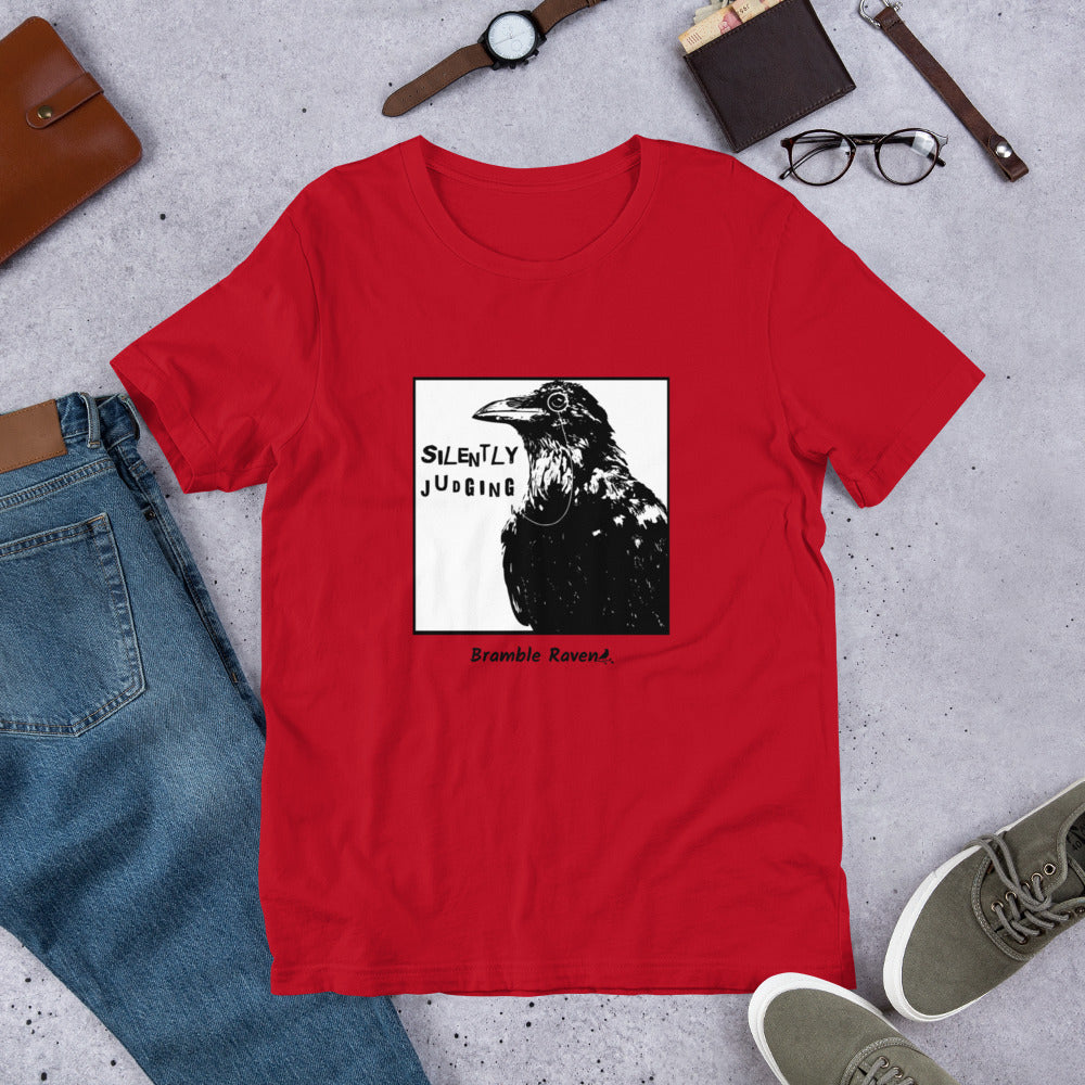 Unisex red colored t-shirt. Features silently judging text next to black crow wearing a monocle in a square frame on a white background. 