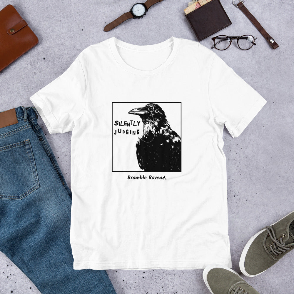 Unisex white colored t-shirt. Features silently judging text next to black crow wearing a monocle in a square frame on a white background. 