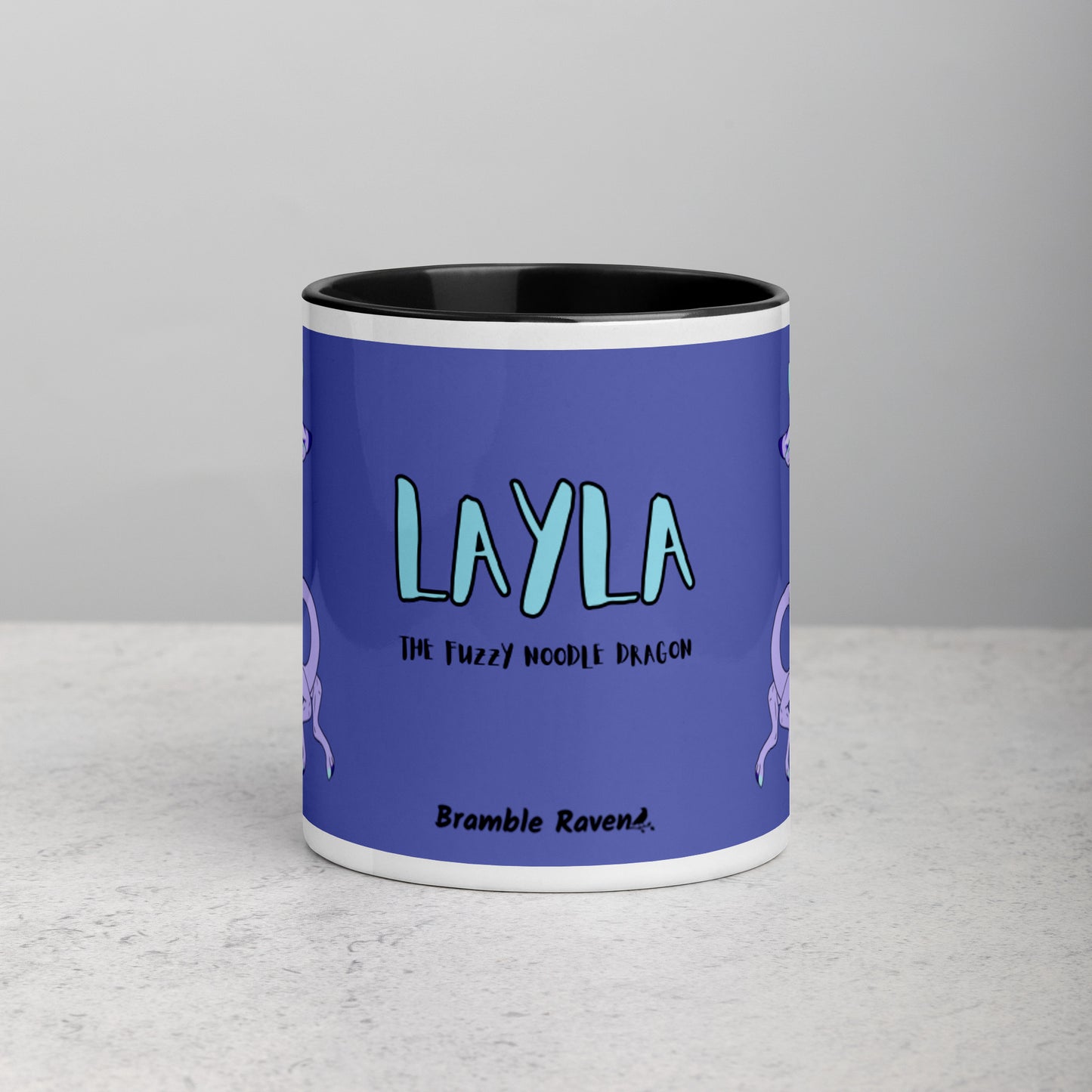 11 ounce white ceramic mug. Black inside and handle. Features double-sided image of Layla the Lavender Fuzzy Noodle Dragon. Shown on tabletop. Front view shows Layla the Fuzzy Noodle Dragon text and Bramble Raven logo.