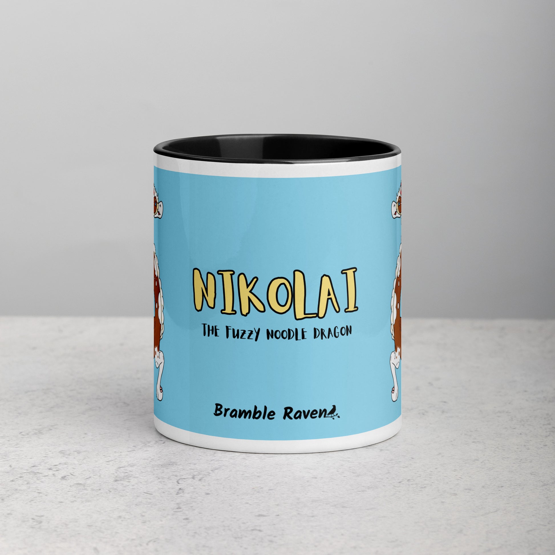 11 ounce ceramic mug with black handle, rim and inside color. Features double-sided image of Nikolai the Fuzzy Noodle Root beer float dragon on a light blue background. Mug is microwave and dishwasher safe. Front view shows Nikolai the Fuzzy Noodle Dragon text and Bramble Raven logo.
