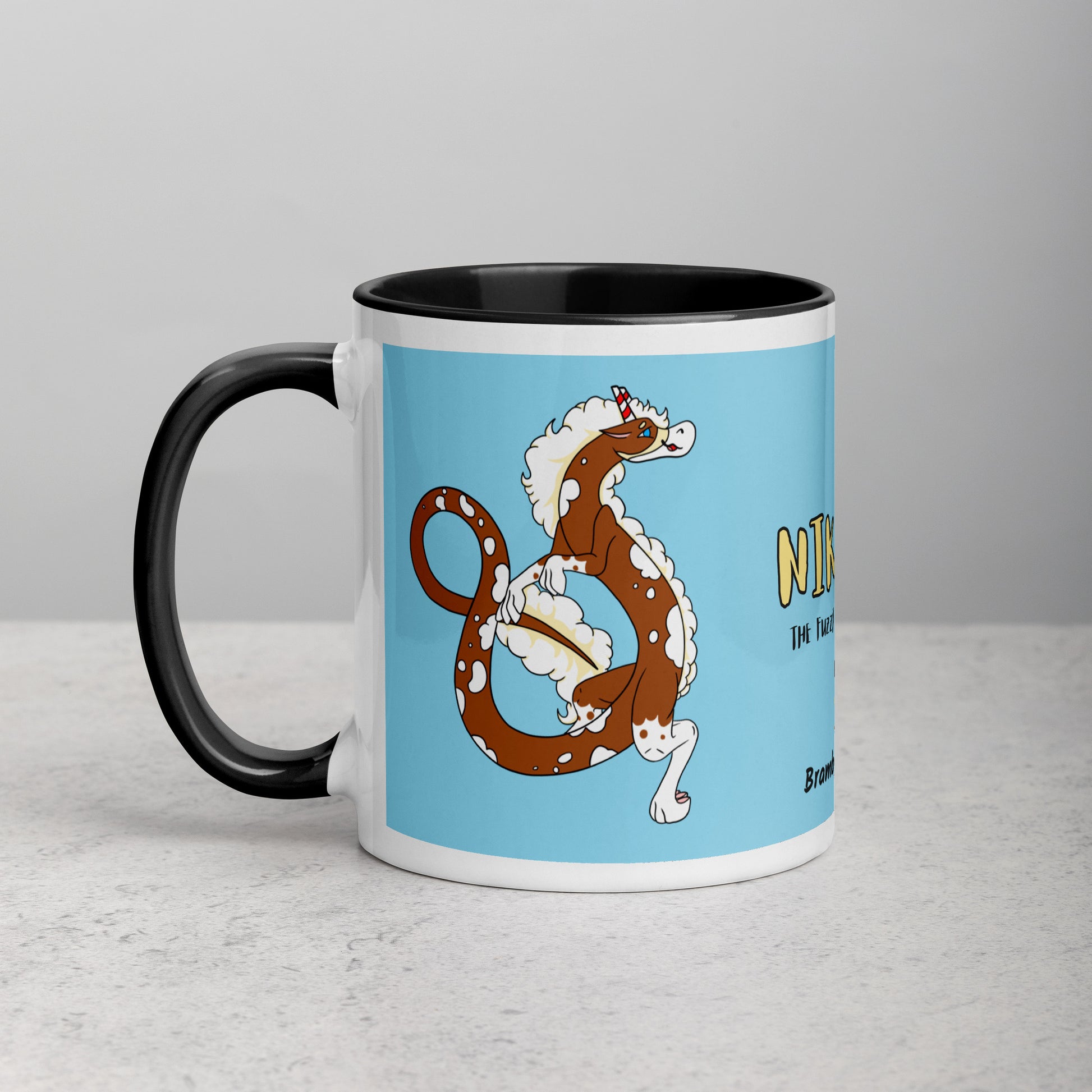 11 ounce ceramic mug with black handle, rim and inside color. Features double-sided image of Nikolai the Fuzzy Noodle Root beer float dragon on a light blue background. Mug is microwave and dishwasher safe.