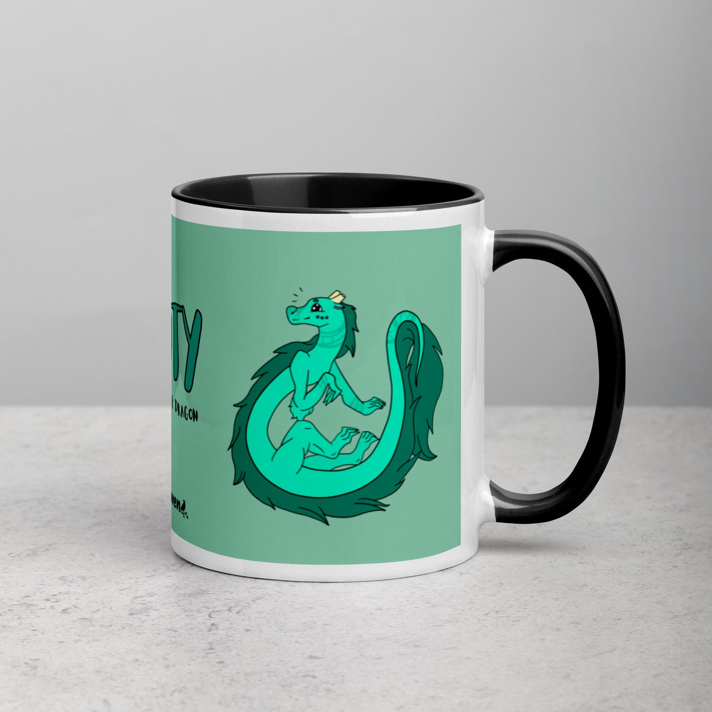 11 ounce white ceramic mug. Black inside and handle. Features double-sided image of Minty the Fuzzy Noodle Dragon on a green background. Shown on tabletop with handle facing right.