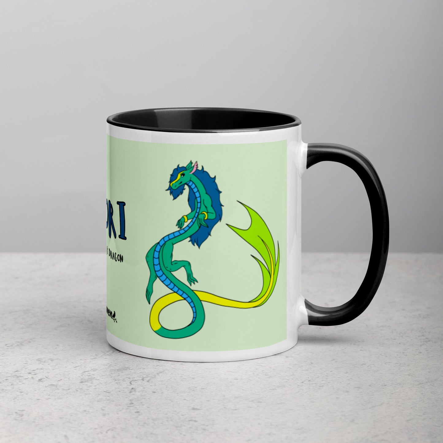 11 ounce white ceramic mug. Black inside and handle. Features double-sided image of Mikori the Fuzzy Noodle Dragon. Shown on tabletop with handle facing right.