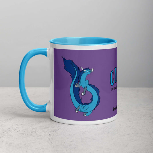 11 ounce white ceramic mug featuring a double-sided image of  Cirri the Fuzzy Noodle Dragon against a purple background.  Blue inside and handle. Shown on tabletop.