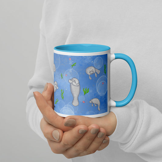 This 11 ounce mug features a wrap-around design of cute manatees, seashells, seaweed and bubbles on a blue background. Has a blue handle, rim, and inside color. This mug is microwave and dishwasher safe. Shown in model's hands.
