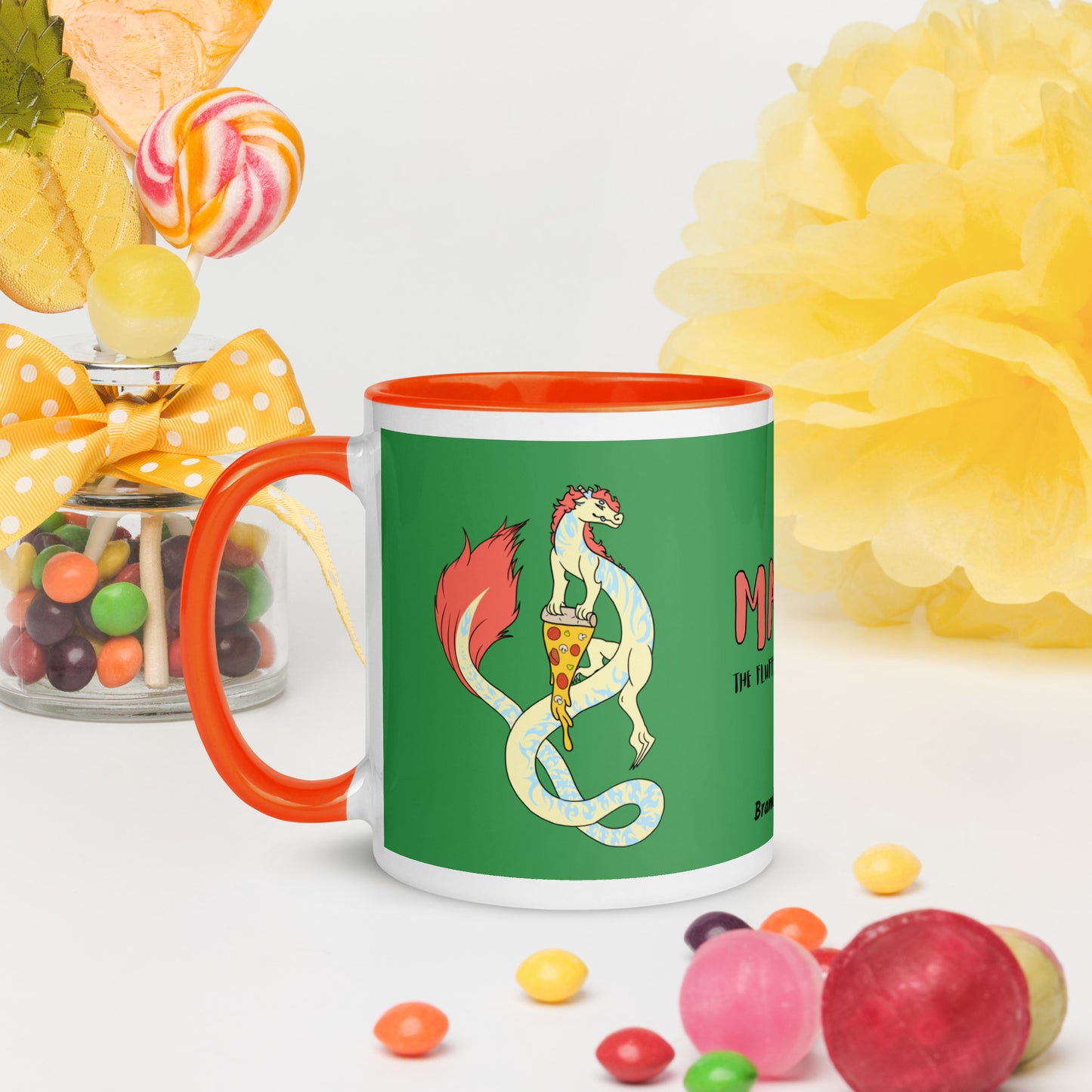 11 ounce white ceramic mug. Orange inside and handle. Features double-sided image of Maisy the Fuzzy Noodle Dragon with a slice of pizza. Shown surrounded by candies and decorations.