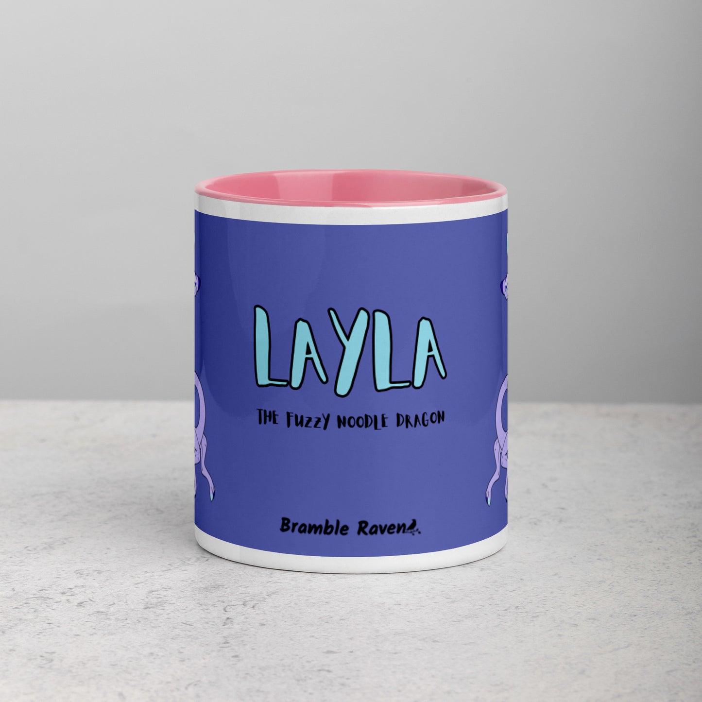 11 ounce white ceramic mug. Pink inside and handle. Features double-sided image of Layla the Lavender Fuzzy Noodle Dragon. Shown on tabletop. Front view shows Layla the Fuzzy Noodle Dragon text and Bramble Raven logo.
