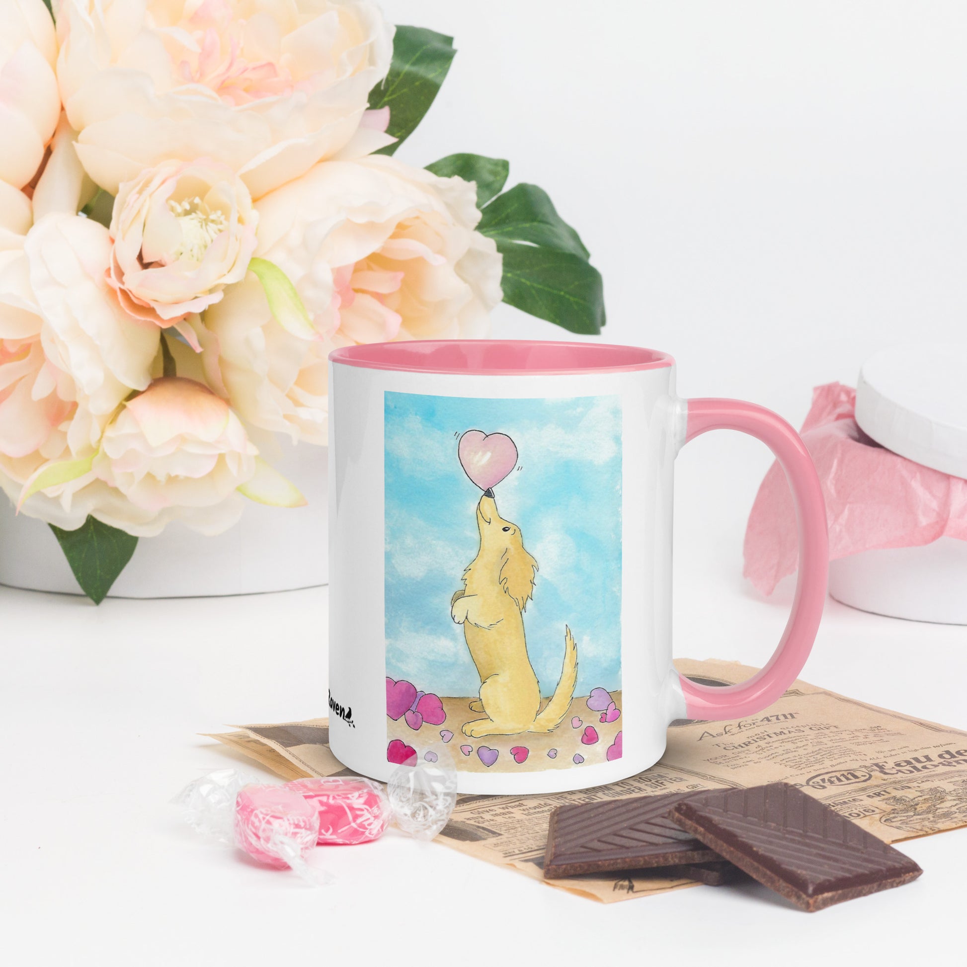 11 ounce ceramic mug featuring Puppy Love watercolor design of a dog and hearts. Double-sided print. Dishwasher and microwave safe. Pink handle, rim and inside. Shown by flowers and chocolates.