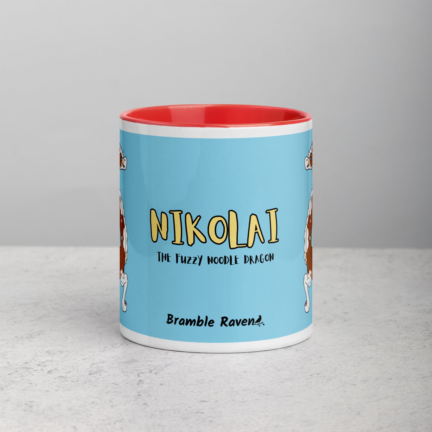 11 ounce ceramic mug with red handle, rim and inside color. Features double-sided image of Nikolai the Fuzzy Noodle Root beer float dragon on a light blue background. Mug is microwave and dishwasher safe. Front view shows Nikolai the Fuzzy Noodle Dragon text and Bramble Raven logo.