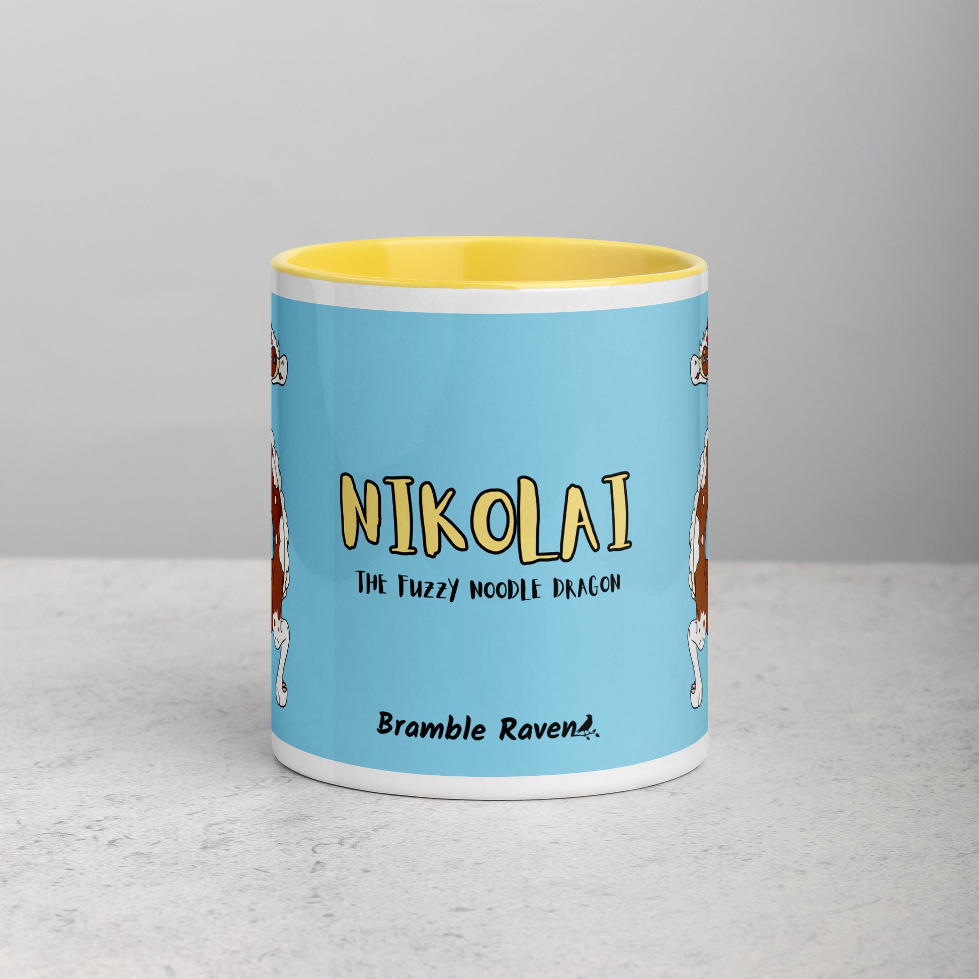 11 ounce ceramic mug with yellow handle, rim and inside color. Features double-sided image of Nikolai the Fuzzy Noodle Root beer float dragon on a light blue background. Mug is microwave and dishwasher safe. Front view shows Nikolai the Fuzzy Noodle Dragon text and Bramble Raven logo.