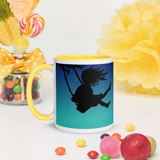 Original Swing Free design of a girl's silhouette in a tree swing against the backdrop of a blue starry sky. Double image on 11 ounce ceramic mug with yellow inside and on handle. Mug surrounded by candy and decorations. Image  with mug handle to the left.