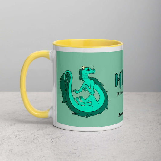 11 ounce white ceramic mug. Yellow inside and handle. Features double-sided image of Minty the Fuzzy Noodle Dragon on a green background. Shown on tabletop.