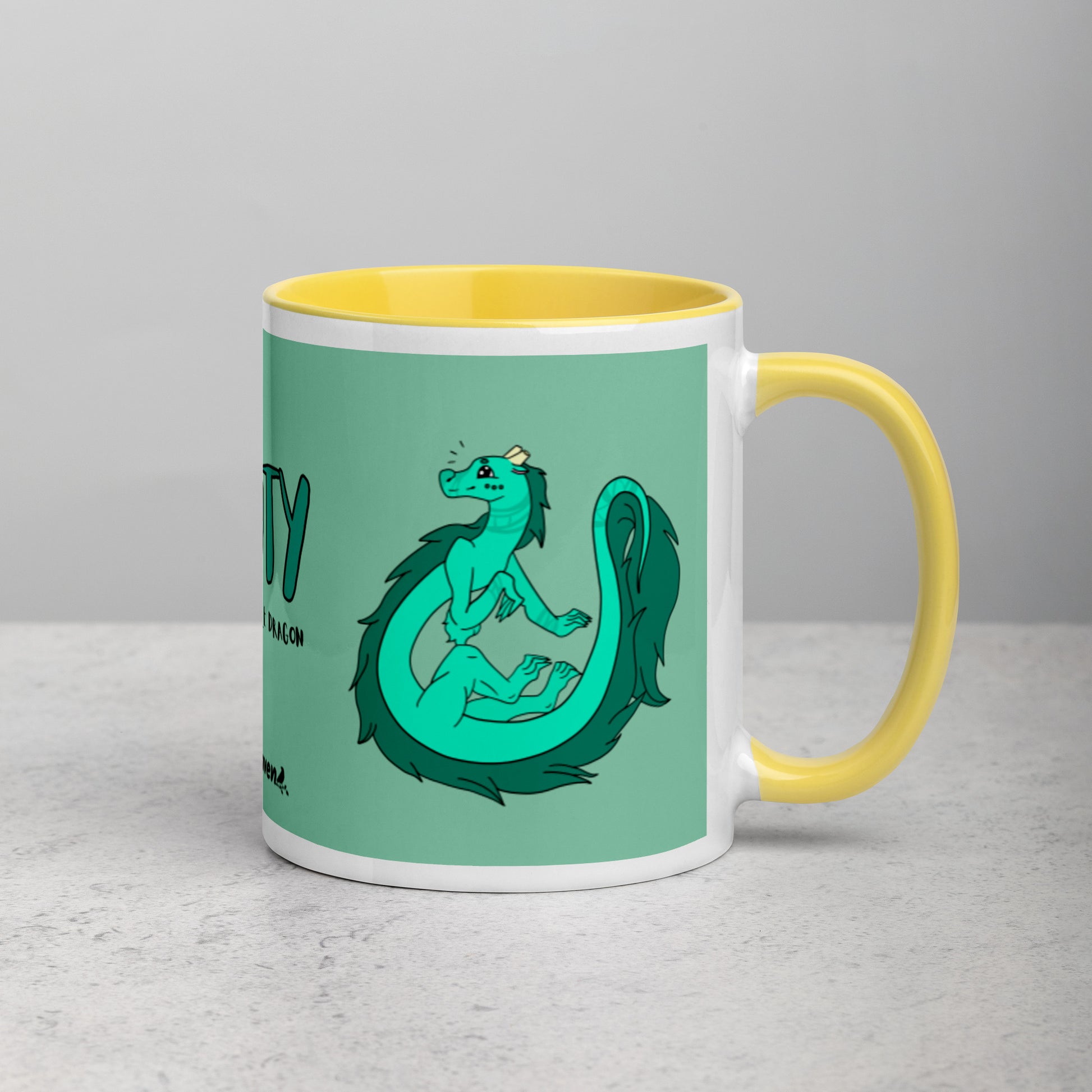 11 ounce white ceramic mug. Yellow inside and handle. Features double-sided image of Minty the Fuzzy Noodle Dragon on a green background. Shown on tabletop with handle facing right.