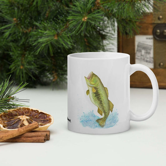 White glossy 11 oz mug. Features a watercolor painting of a largemouth bass leaping out of the water. Double sided design. Shown by pine boughs, dried citrus slices and cinnamon sticks.