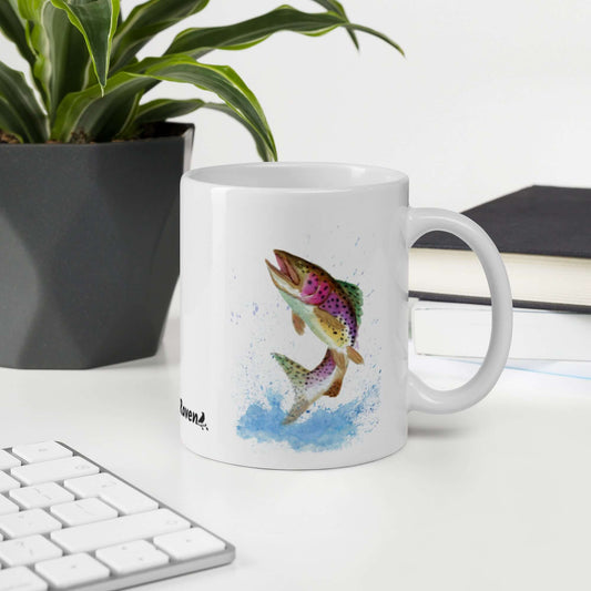 White glossy 11 oz mug. Features original watercolor painting of a rainbow trout leaping from the water. Double-sided design. Shown on a desk by a potted plant.