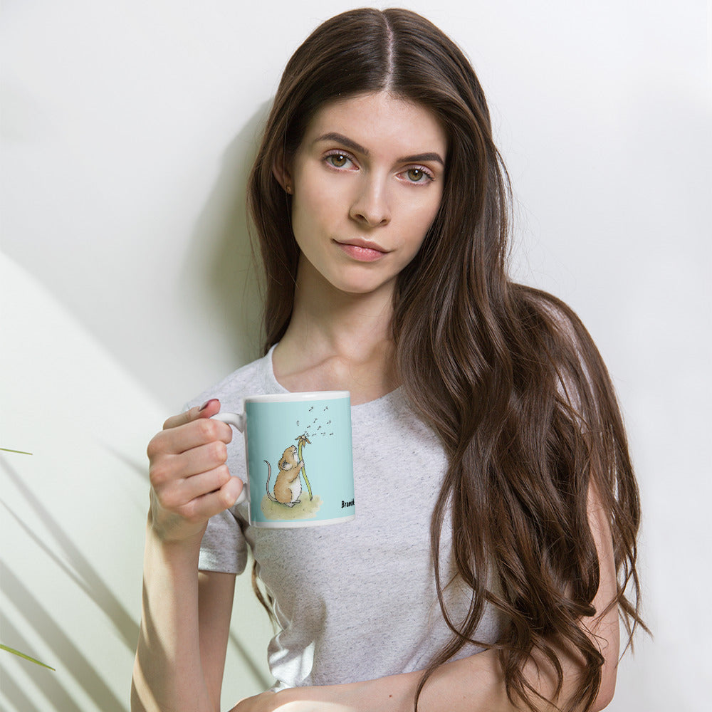 Two-sided image of original Dandelion wish design of cute watercolor mouse blowing dandelion seeds  featured on 11 ounce mug with light blue background. Held in the hand of a female model.