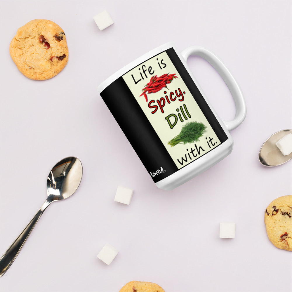 15 ounce white glossy ceramic mug. Life is Spicy. Dill with it text. Image of chili peppers and dill weed on a light yellow rectangle. Black background on mug. Shown on table surrounded by chocolate chip cookies, sugar cubes and spoons.